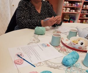 mains en train de crocheter | pelote bleue | crochet bleu | feuille papier explicative de l'ouvrage en cours