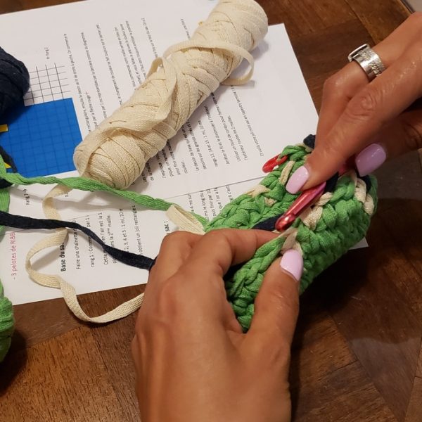 Deux mains en appui sur une table en train de crocheter un début d'ouvrage de couleur verte.