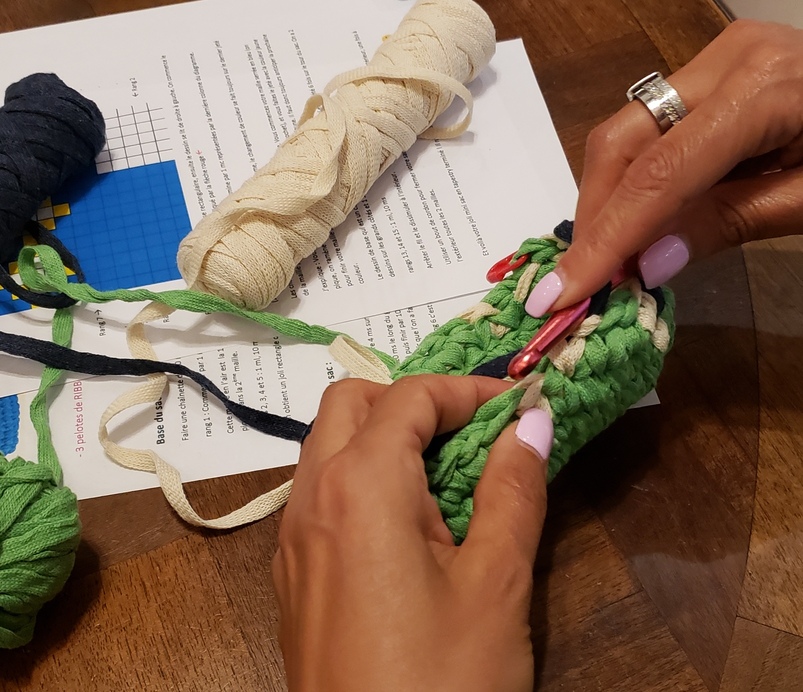 Deux mains en appui sur une table en train de crocheter un début d'ouvrage de couleur verte.